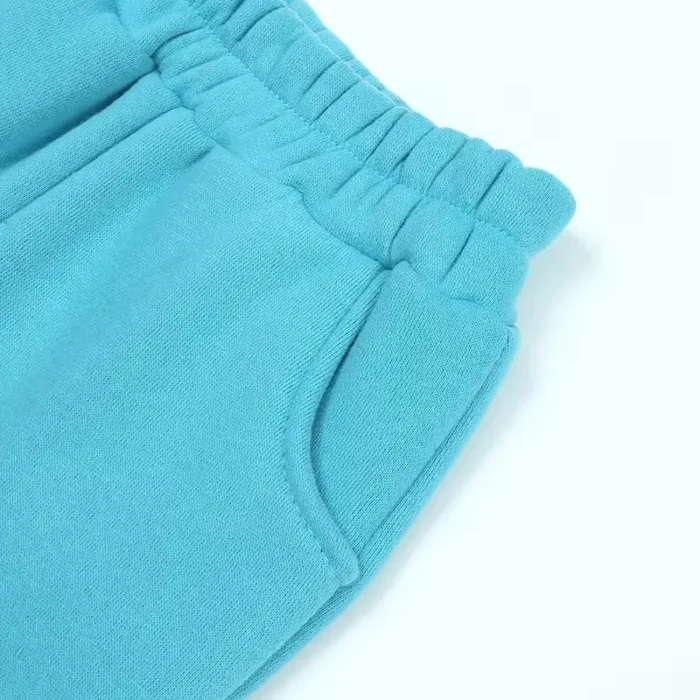 Close-up of custom baby joggers side detail, showing premium elastic waistband construction, reinforced curved pockets, and high-density cotton fleece fabric. Professional infant sweatpants manufacturing by an expert clothing factory.