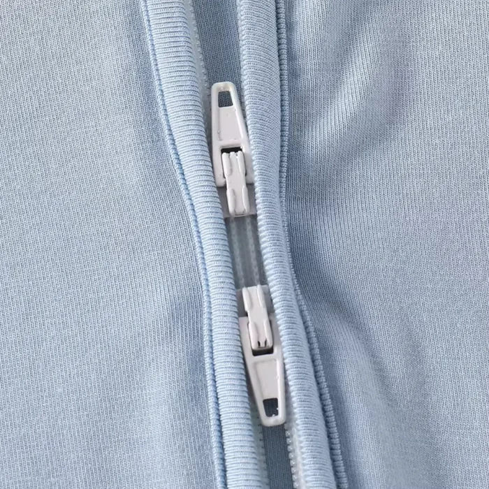 Close-up of baby romper two-way zipper system, featuring dual high-quality sliders for flexible top or bottom access. Premium functional infant jumpsuit hardware from a professional clothing manufacturer.
