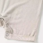 Close-up of baby romper crotch snaps, featuring durable nickel-free metal snap buttons for easy diaper changes and reinforced fabric plackets. High-quality infant apparel hardware from a professional clothing manufacturer.