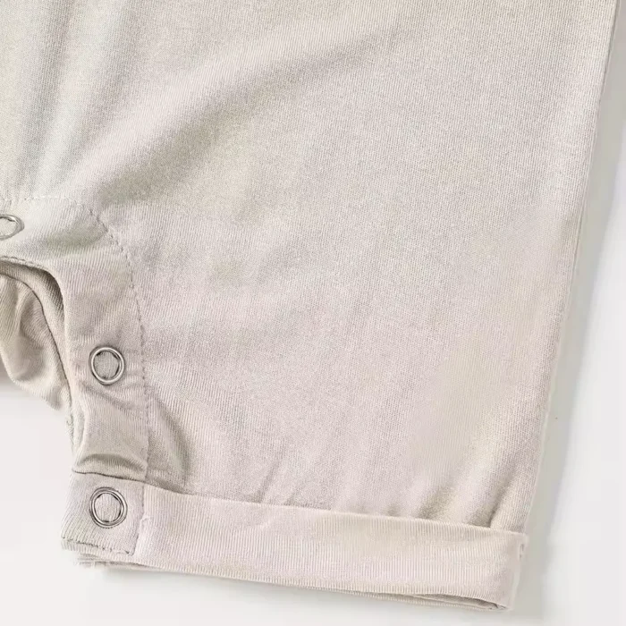 Close-up of baby romper crotch snaps, featuring durable nickel-free metal snap buttons for easy diaper changes and reinforced fabric plackets. High-quality infant apparel hardware from a professional clothing manufacturer.