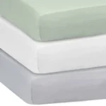 Stack of solid color crib sheets in sage green, white, and gray from an OEM crib sheets factory in China.