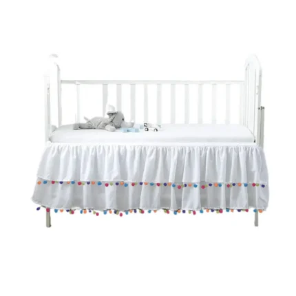 White pom pom crib skirt with colorful tassels, manufactured by a professional crib skirts factory in China.