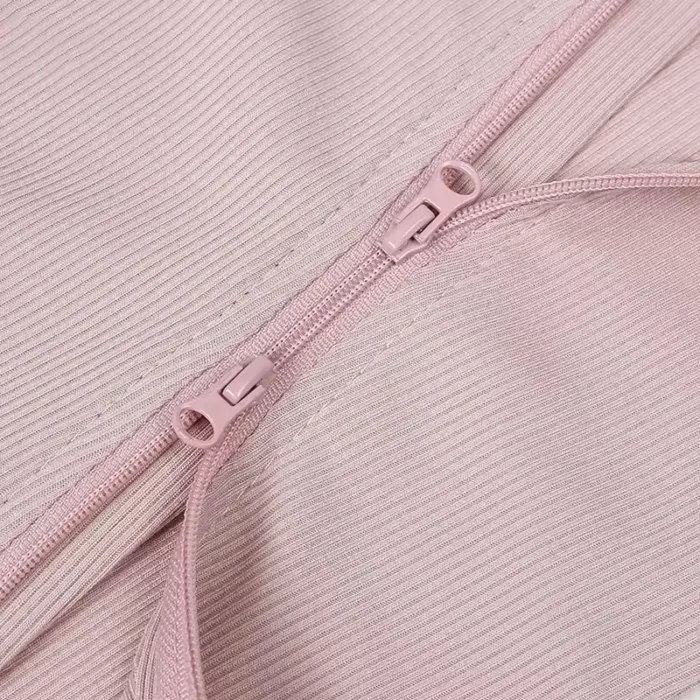 Close-up of a high-quality two-way zipper on a pink baby romper, showcasing smooth sliding functionality and tonal matching color. Essential functional infant sleepwear hardware from a professional clothing manufacturer.