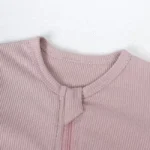 Close-up of baby romper neckline, featuring a protective fabric zipper guard, soft-bound round neck, and premium pink ribbed cotton fabric. High-quality infant safety construction from a professional clothing manufacturer.