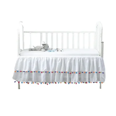 White pom pom crib skirt with colorful tassels, manufactured by a professional crib skirts factory in China.